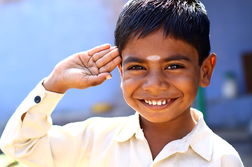 Funny Indian kid giving salute in outdoor background.