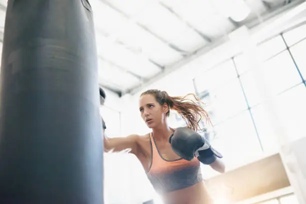 Shot of an attractive young woman working out with a punching bag at the gym