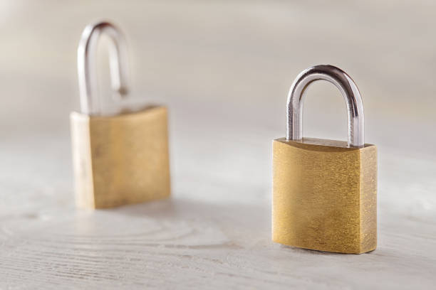 istock Two padlock, lock and unlock, with silvered keys on white wooden background. Estate and security concept with symbol of protection. 936792968