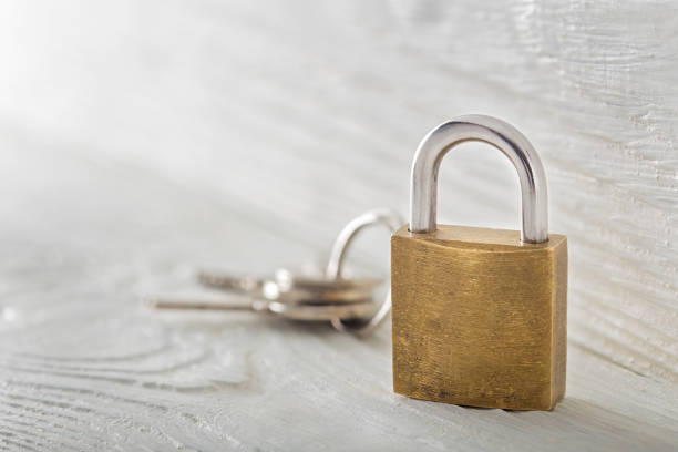 istock Locked padlock with silvered keys on white wooden background. Estate and security concept with symbol of protection. 936792998