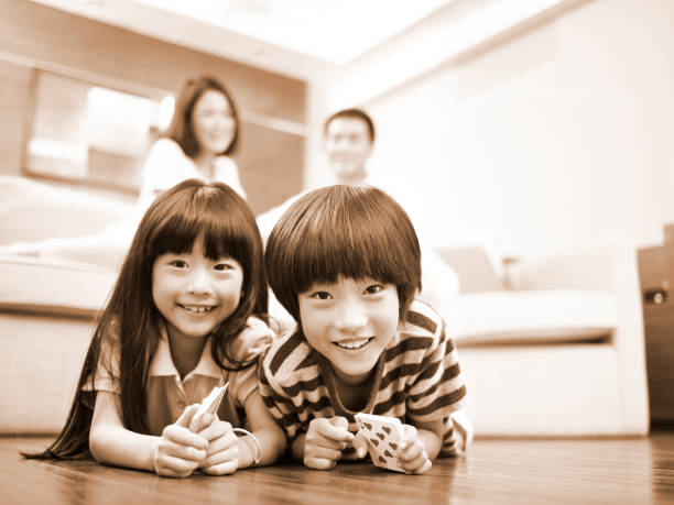 asian brother and sister lying on front on floor with parents in the background, black and white sepia.
