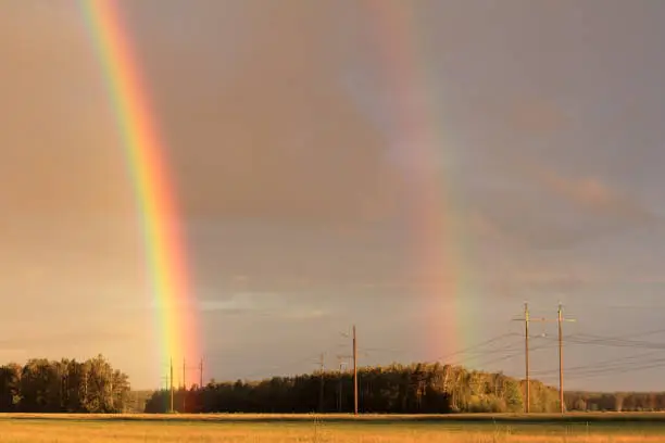 double rainbow after the rain against the backdrop of fields, forests, power lines