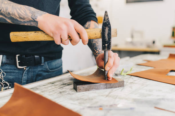 istock Close up of a leather craftsman working with leather using hammer. 936801838