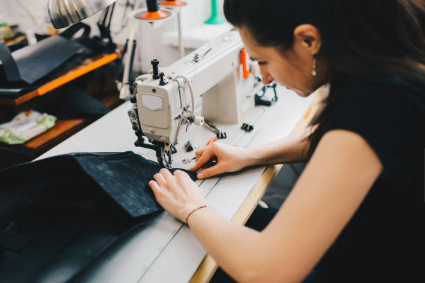 istock Female artisan threading black leather on sewing machine, close up 936804158