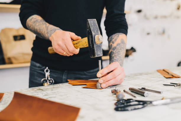 istock Close up of a leather craftsman working with leather using hammer. Working process in the leather workshop. Man holding crafting tool and working. 936804314
