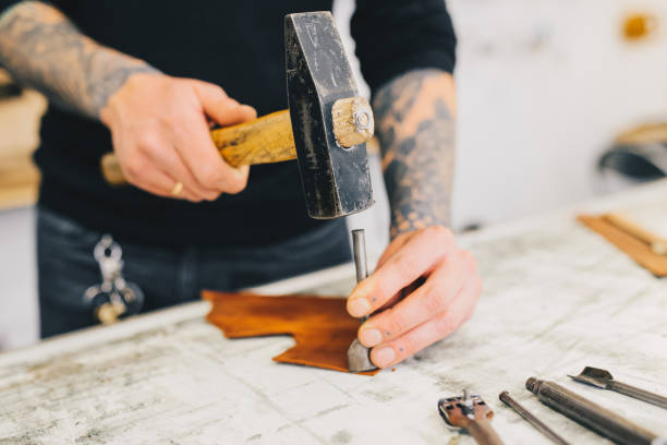 istock Close up of a leather craftsman working with leather using hammer. Working process in the leather workshop. Man holding crafting tool and working. 936804316
