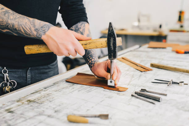 istock Close up of a leather craftsman working with leather using hammer. Working process in the leather workshop. Man holding crafting tool and working. 936804354