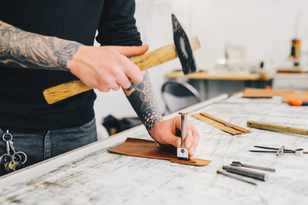 istock Close up of a leather craftsman working with leather using hammer. Working process in the leather workshop. Man holding crafting tool and working. 936804376
