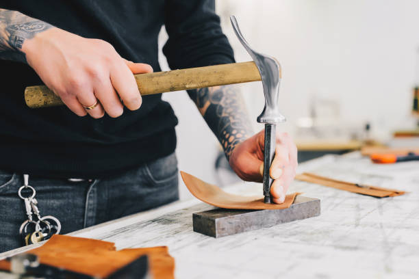 istock Close up of a leather craftsman working with leather using hammer. Working process in the leather workshop. Man holding crafting tool and working. 936804418