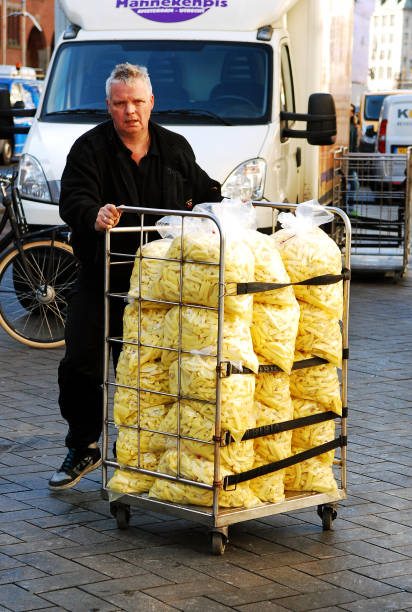 Man making a delivery of a lorry fully loaded with bags of raw french fries to a Restaurant in the Damrak street of Amsterdam.\nKnown to the world as French fries, not many people know that the best fries are to be eaten in Holland and Belgium. Amsterdam is home to several places exclusively serving these delicious chips, known as Patat or Flaamse frites.