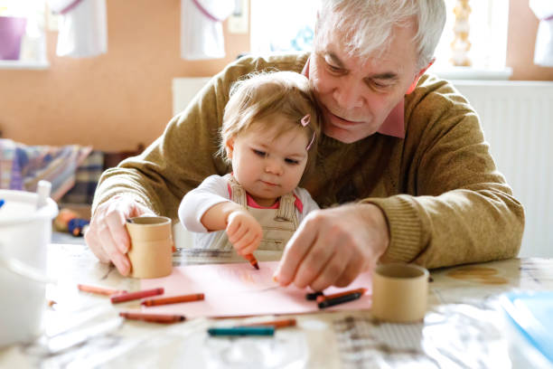 süße kleine baby kleinkind mädchen und gut aussehend senior großvater malerei mit bunten bleistiften zu hause. enkelkind und man gemeinsam spaß haben - grandparent grandfather granddaughter little girls stock-fotos und bilder