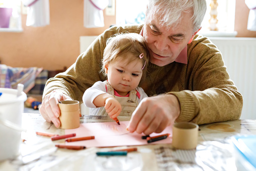 Lindo pequeño bebé niño niña y abuelo senior guapo pintura con lápices de colores en el hogar. Nieto y el hombre que se divierten juntos photo