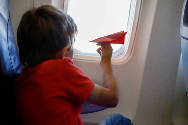 istock Little kid boy playing with red paper plane during flight on airplane 936817770