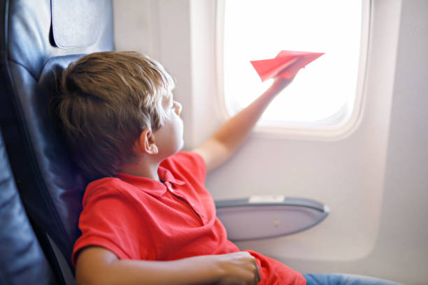 Mały chłopiec bawiąc się czerwonym papierowym samolotem podczas lotu samolotem – zdjęcie