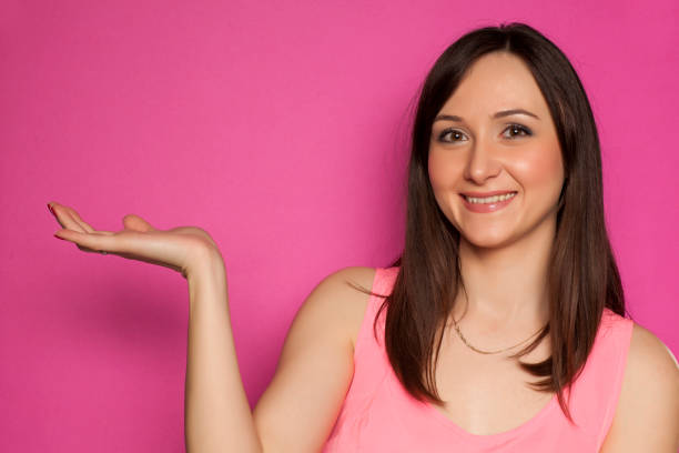 istock Young smiling woman holding imaginary object on pink background 936821866