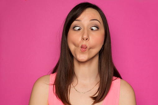 Young funny woman making silly faces on pink background