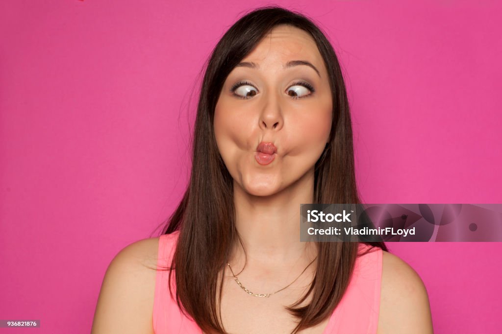 Young funny woman making silly faces on pink background Women Stock Photo