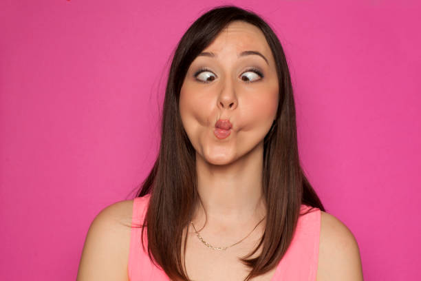 Young funny woman making silly faces on pink background Young funny woman making silly faces on pink background grimacing stock pictures, royalty-free photos & images