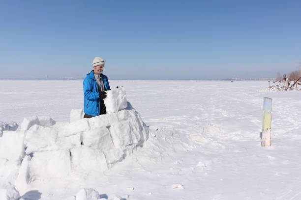 istock Man in a blue jacket building an igloo on a glade in the winter 936822246
