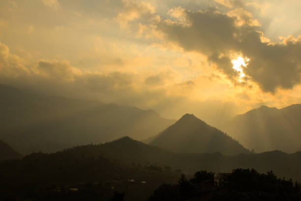 istock sun ray and sun light shining through clouds hitting layers of mountains, drawing a very impressive silhouette photo in warm feeling. 936822322