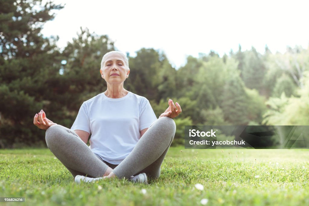 Calm peaceful woman meditating Peace and relaxation. Calm nice peaceful woman sitting on the grass and closing her eyes while meditating Yoga Stock Photo