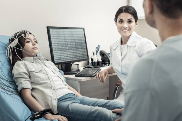 Nice positive doctor sitting in front of the computer Professional neurologist. Nice positive female doctor sitting in front of the computer and smiling while looking at her patients eeg stock pictures, royalty-free photos & images