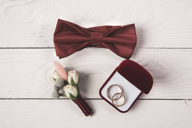 flat lay with invitation, buttonhole, bow tie and jewelry box on wooden surface flat lay with invitation, buttonhole, bow tie and jewelry box on wooden surface buttonhole flower stock pictures, royalty-free photos & images