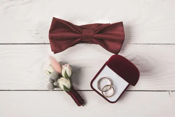 flat lay with invitation, buttonhole, bow tie and jewelry box on wooden surface
