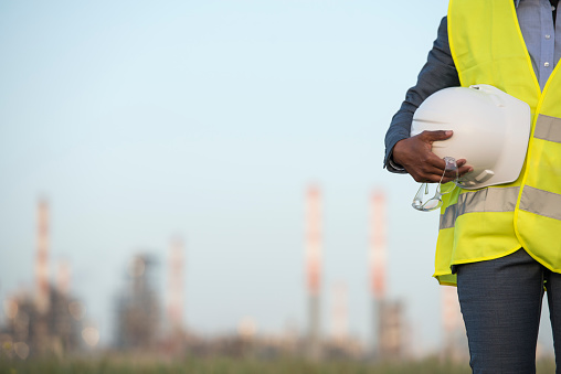 Chemical plant technician outdoors. Selective focus on the unrecognisable worker in reflective vest holding safety helmet, protective glasses.