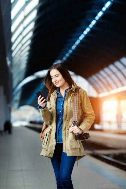 istock Beautiful young woman using smart-phone while standing on the railway station platform. 936841612
