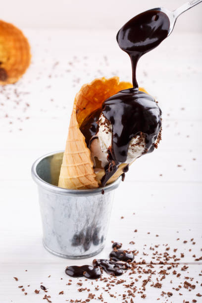istock Homemade vanilla ice-cream with chocolate topping in waffle cone on white table. 936842136