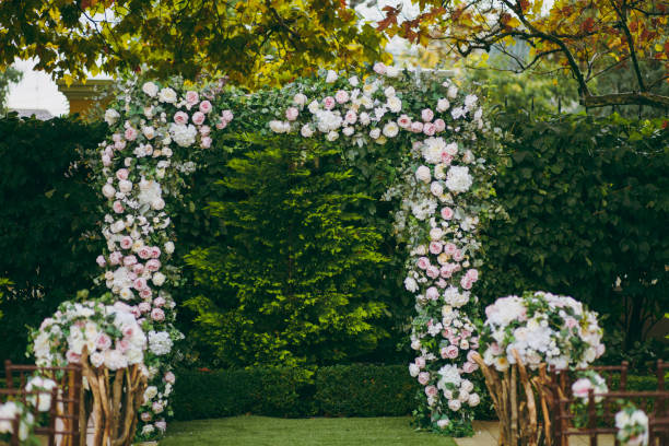 istock Beautiful decoration of a wedding ceremony in a green autumn garden. Rectangular arch, adorned with delicate pink and cream peonies and green leaves next to flower compositions on branches 936843134