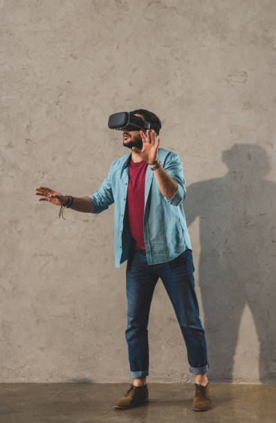 istock Young man standing in front of wall and using virtual reality headset 936845550