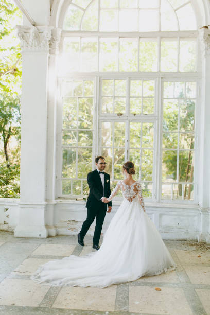 beau mariage photosession. marié en costume noir et jeune mariée en robe de dentelle blanche avec panache long avec une coiffure exquis en intérieur vintage sur la véranda d’une vieille maison avec des colonnes - veil bride lace married photos et images de collection