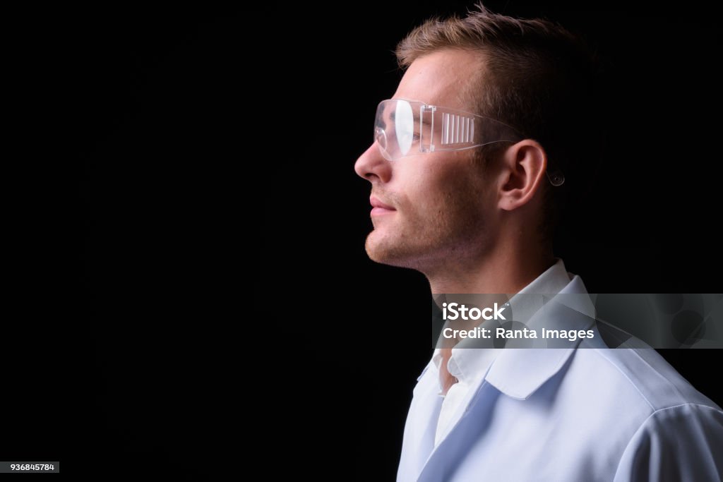 Ritratto di giovane bell'uomo che indossa un camice da laboratorio e occhiali protettivi - Foto stock royalty-free di Scienziato