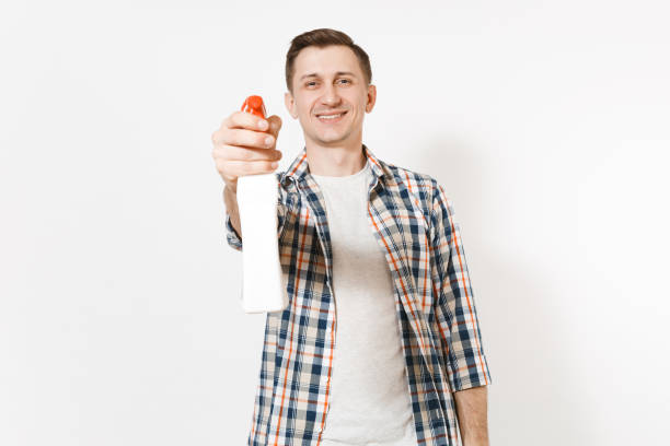 istock Young housekeeper man in checkered shirt holding white blank empty cleaning spray bottle with cleaner liquid isolated on white background. Male doing house chores. Copy space for advertisement. 936849870