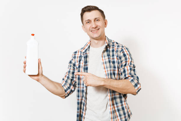istock Young housekeeper man in checkered shirt holding white empty cleaning bottle with cleaner liquid isolated on white background. Male and house chores. Copy space advertisement. Cleanliness concept. 936849880