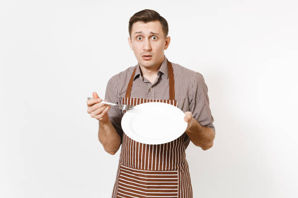 istock Man chef or waiter in striped brown apron, shirt holding white round empty clear plate, fork isolated on white background. Male housekeeper or houseworker. Domestic worker copy space for advertisement 936850268