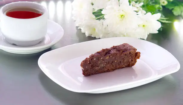 brownie cake on a white plate decorated with chrysanthemum flowers prepared for tea with a mug of tea