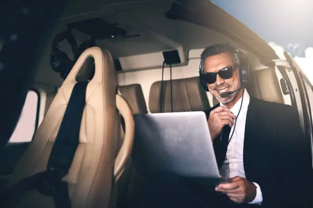 Shot of a mature businessman using a laptop while traveling in a helicopter
