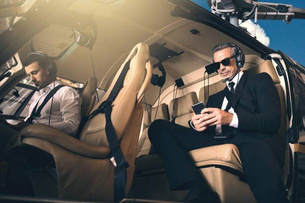 Premium business requires premium transport Shot of a mature businessman using a mobile phone while traveling in a helicopter military private stock pictures, royalty-free photos & images