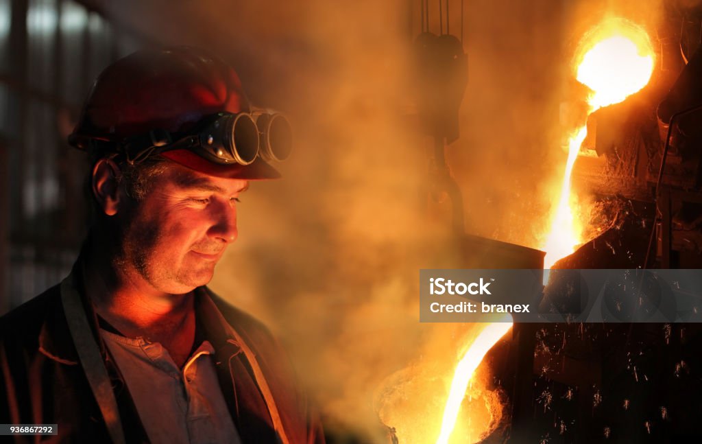 Hard work in the foundry Hard work in the foundry, worker watching and controlling iron smelting in furnaces, too hot and smoky working environment Steel Mill Stock Photo
