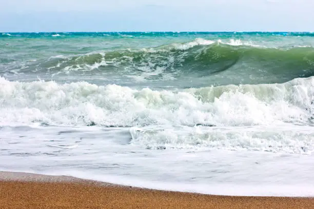 Photo of Stormy sea and blue sky, white sea foam on the yellow sandy beach.