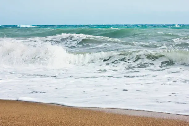 Photo of Stormy sea and blue sky, white sea foam on the yellow sandy beach.