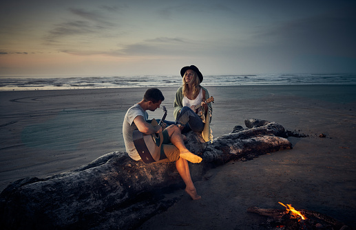 Shot of a young couple playing guitars together while camping along the coast