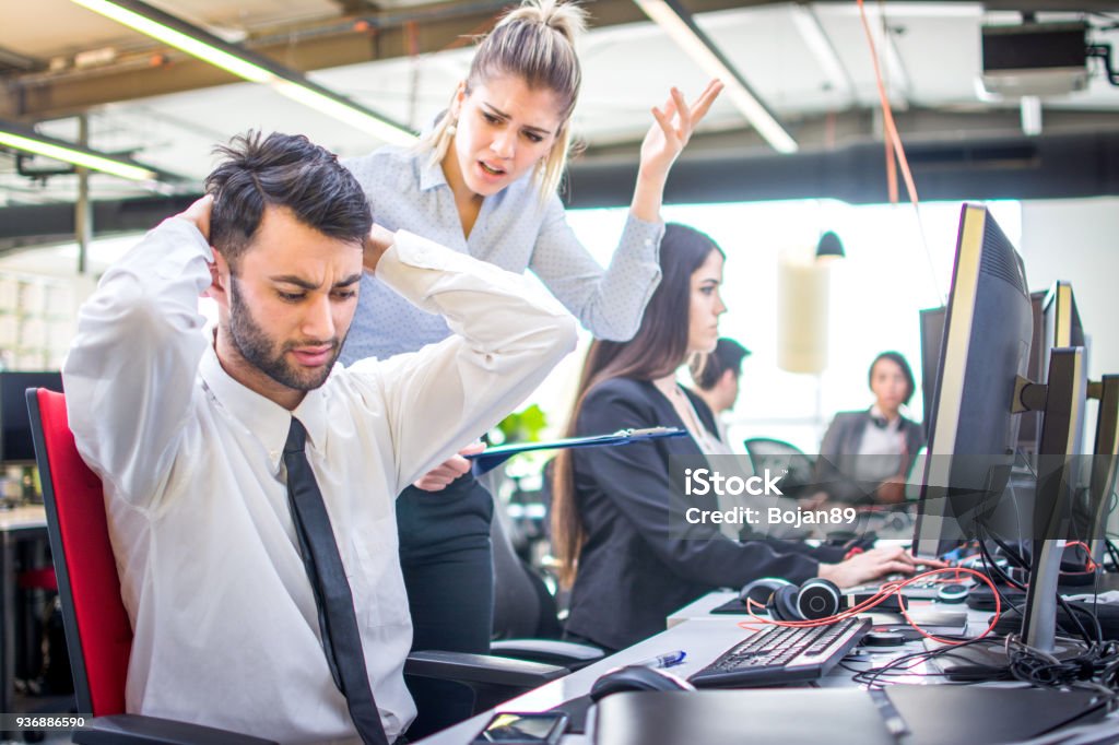 Angry businesswoman shouting at her worker with hands behind head in office Manager Stock Photo