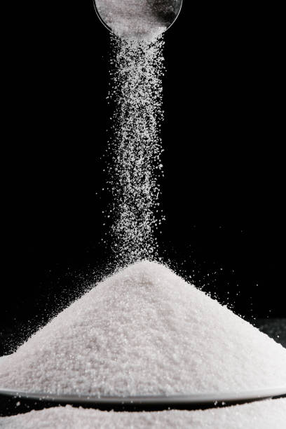 istock sugar falling from metal scoop on pile on plate isolated on black 936890720