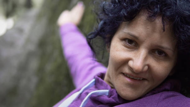 istock Portrait of young woman with short curls smiling and looking at camera while standing leaned on stone in forest, perfect for commercial or video clip 936890964
