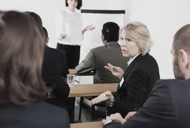 Surprised  stylish mature business woman talking with people during conference in meeting room