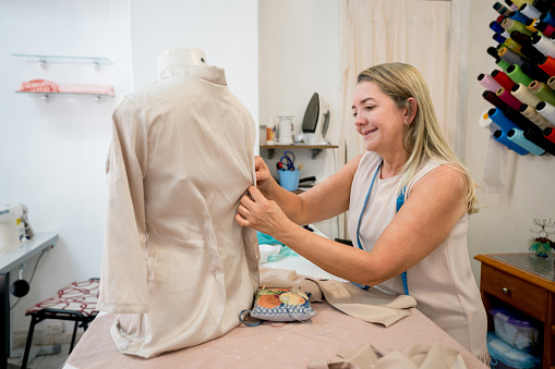 Happy seamstress working at an atelier fitting a shirt on a mannequin - fashion design concepts